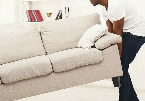 Full length of happy black couple placing sofa in living room of new home. Moving, interior design and real estate concept, copy space